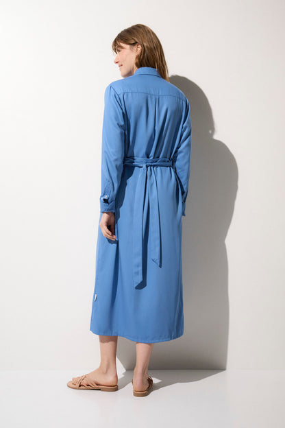 Femme portant une robe chemise anti-UV bleue, élégante et légère, parfaite pour une protection solaire au jardin.