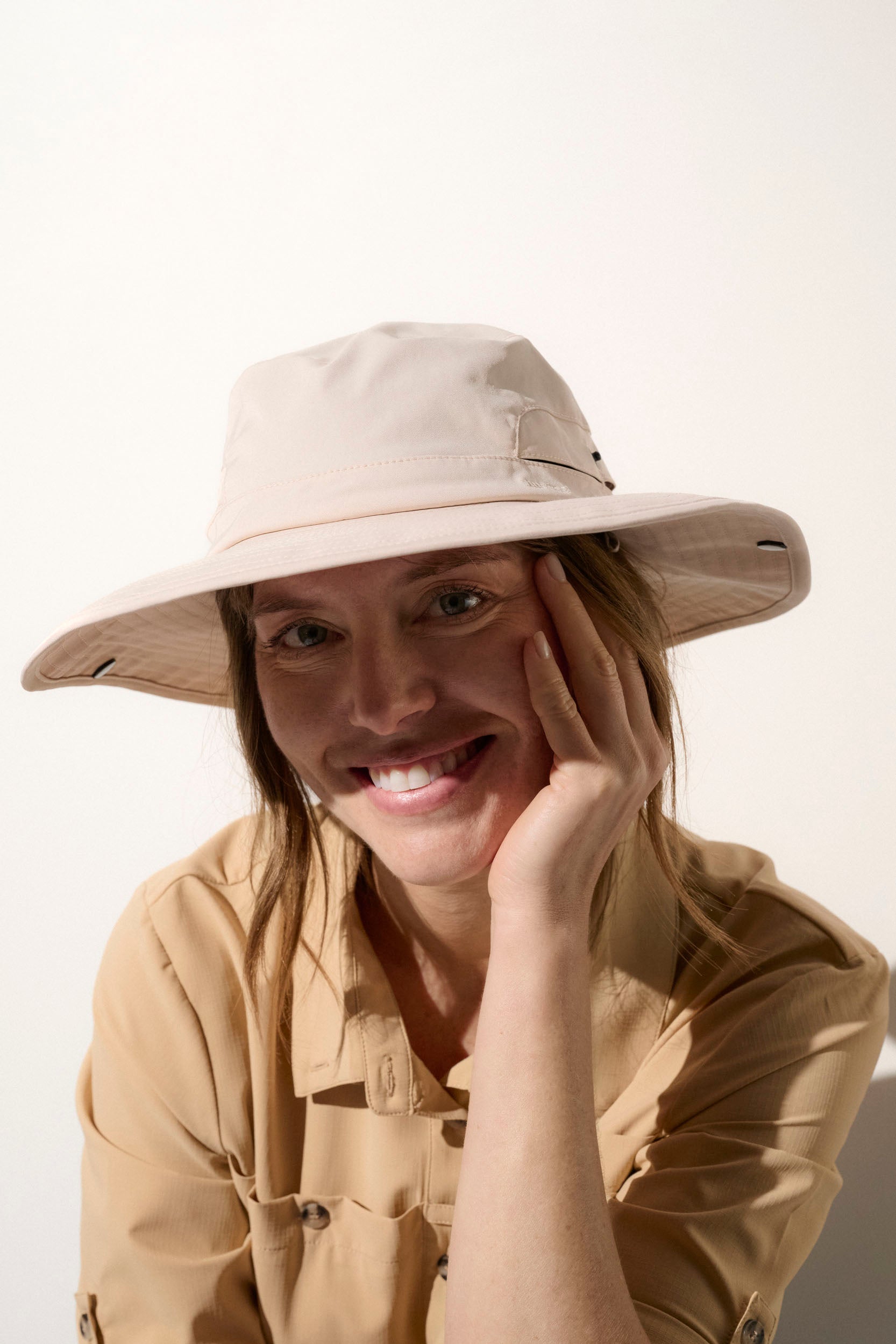 Femme souriante portant un chapeau anti-UV beige UPF50+, idéal pour les randonnées en plein air et la protection solaire.