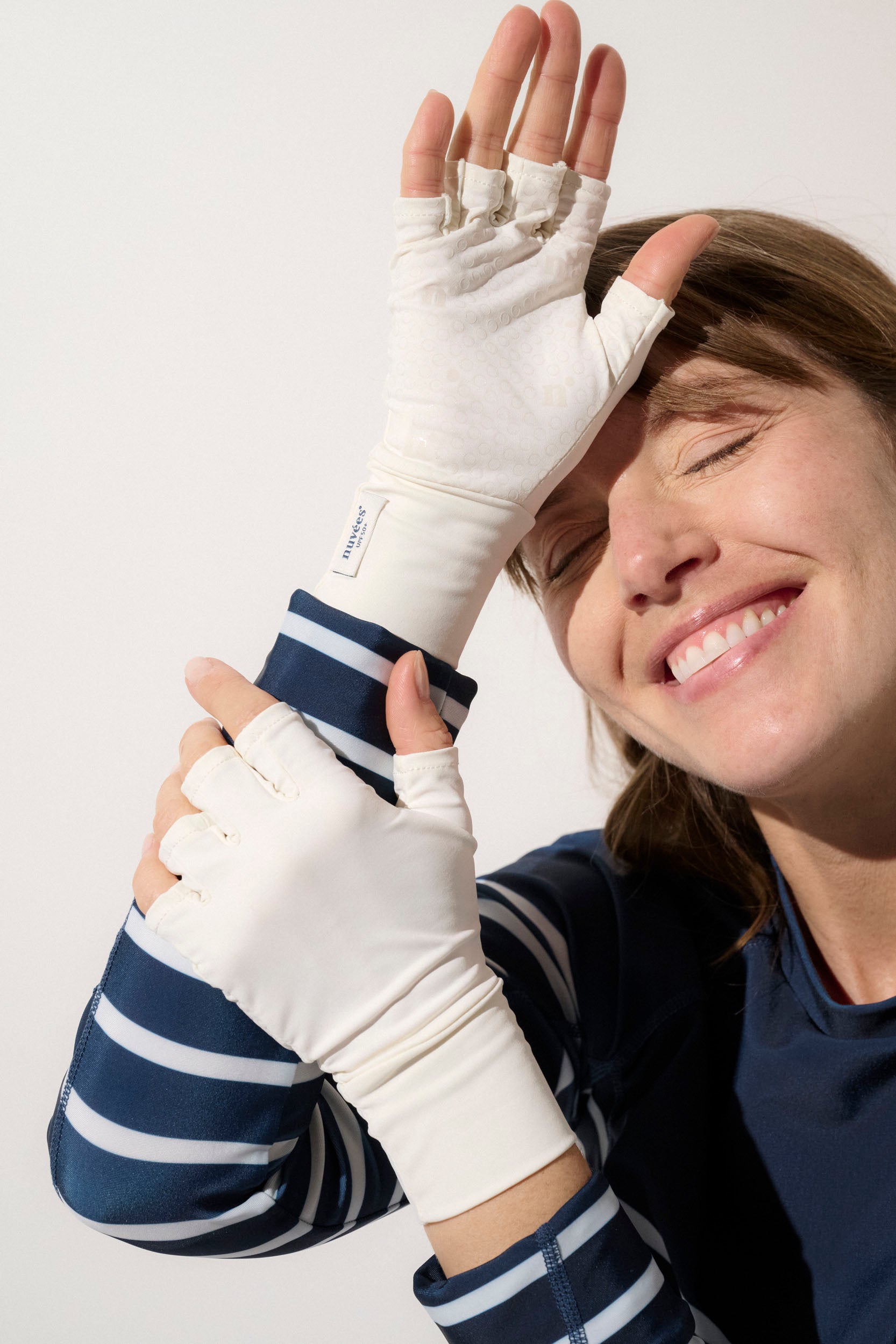 Femme souriante portant des mitaines anti-UV blanches, UPF50+, confortables pour activités extérieures.