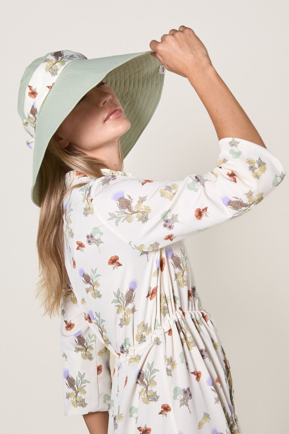 Femme avec chapeau anti-UV Herbe Fraîche, élégant et protecteur, portant une robe fleurie.