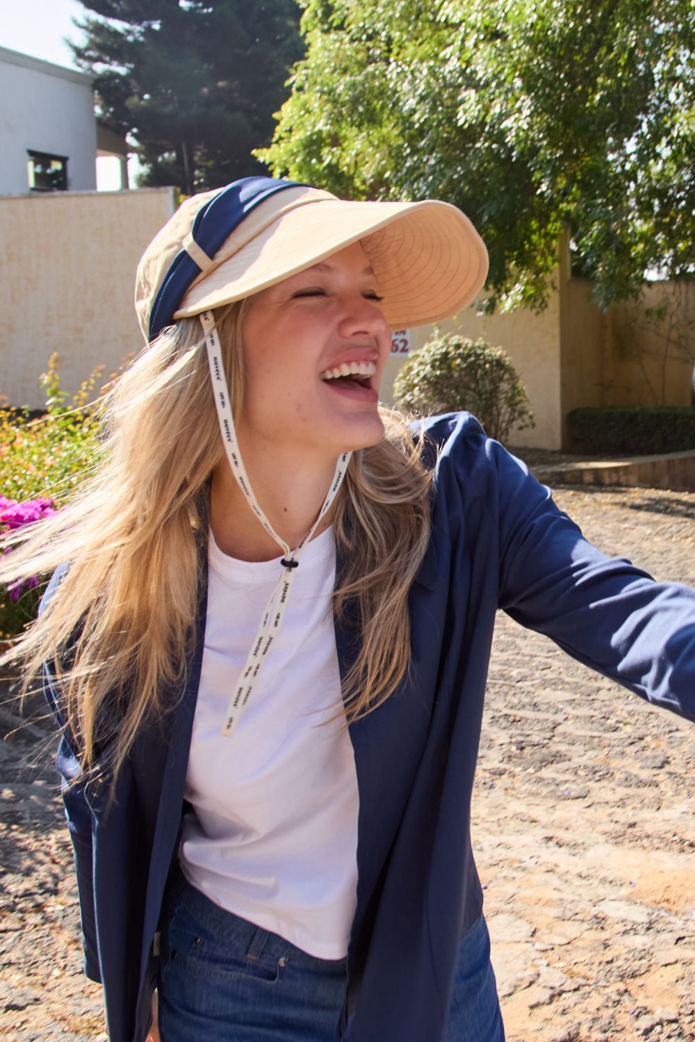 Femme souriante portant un chapeau anti-UV, élégante et protégée du soleil en extérieur.