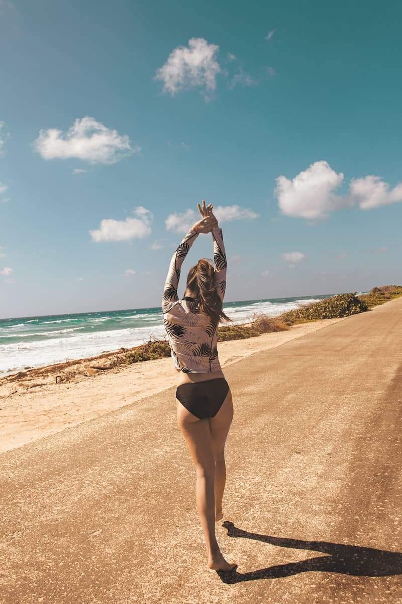 Femme marchant sur la plage en maillot de bain anti-UV noir et haut à manches longues, exposée au soleil.